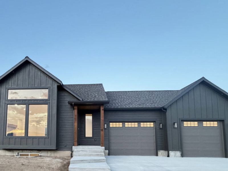 Front exterior at dusk: dark board-and-batten siding, a tall gable window wall, and a two-car garage