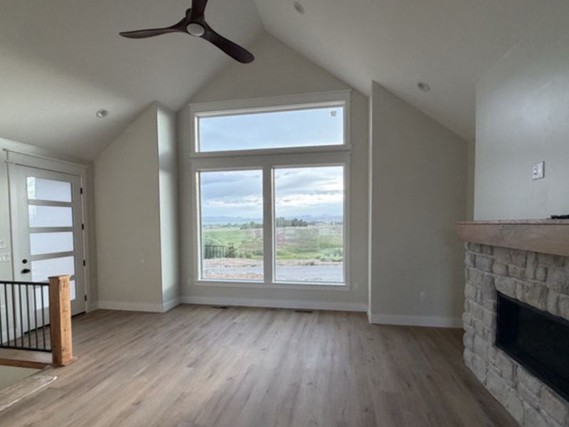 Vaulted great room with a stone fireplace and a wall of windows to the backyard