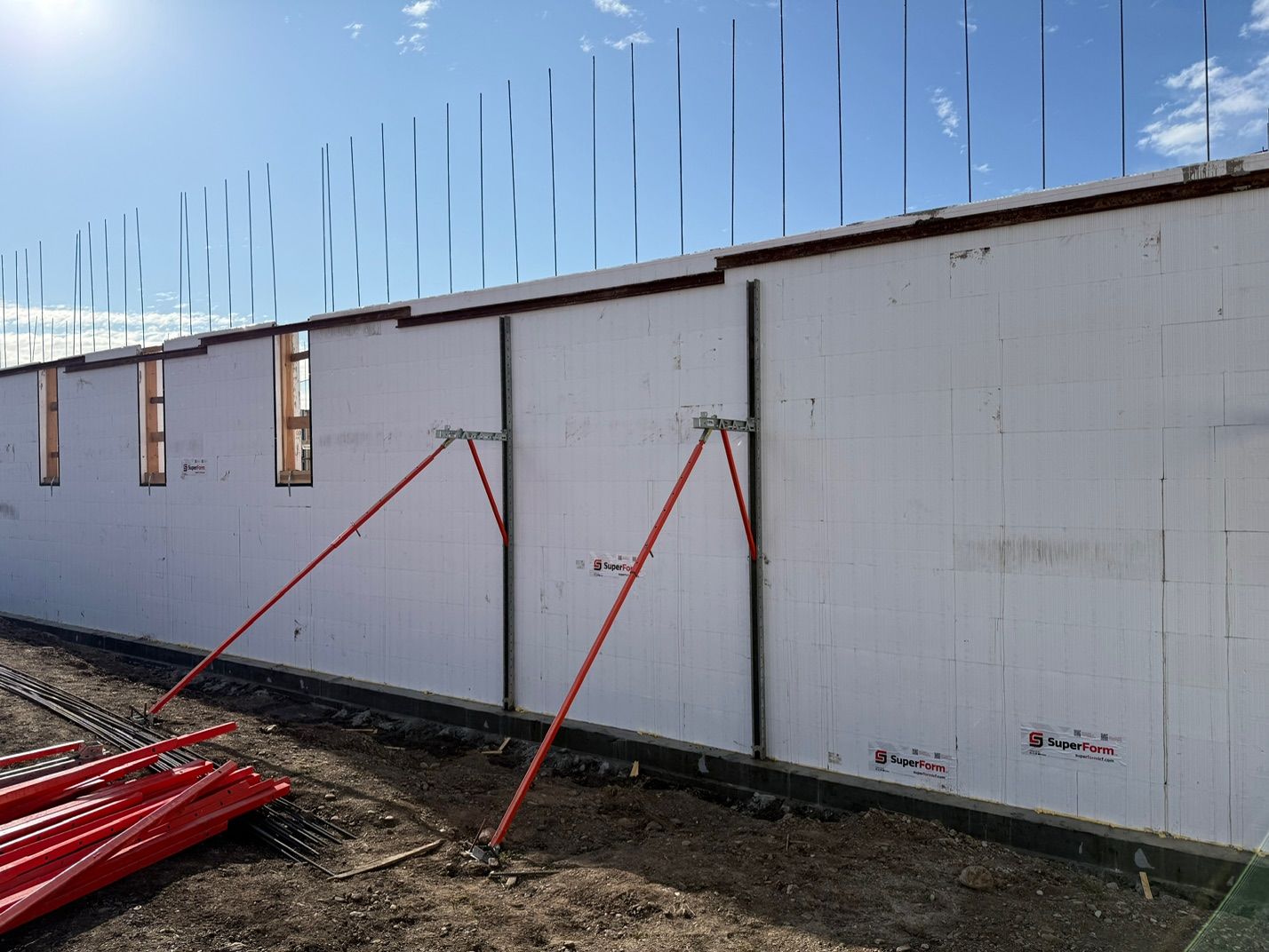 Long white ICF wall held plumb with red alignment braces, vertical rebar extending above