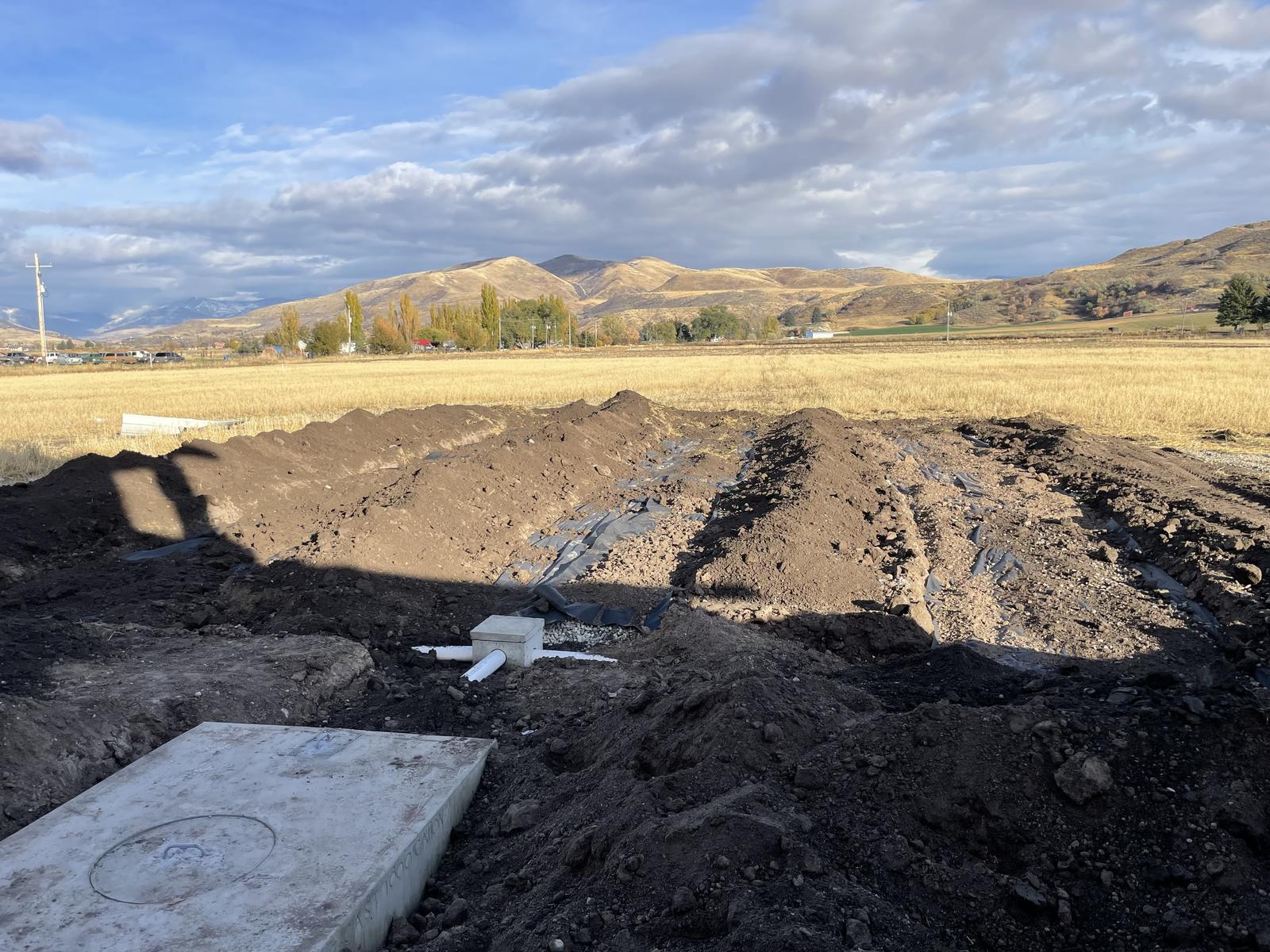 Backfilled drain field in an open field, with a septic tank lid in the foreground and mountains behind